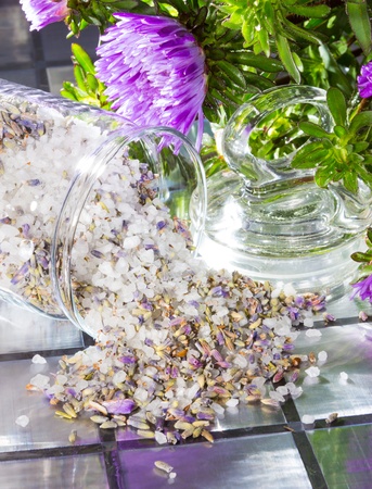 Floral aromatic potpourri with a sweet fragrance made from a mixture of natural flowers, plant shavings and spices spilling out of a glass jar onto a tiled surface with a bunch of fresh purple flowersの写真素材