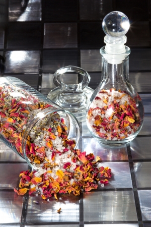 Potpourri with a mixture of colourful dried rose petals, flowers, natural plant shavings and spices spilling out of a glass jar onto a tiled surfaceの写真素材