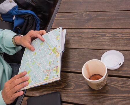 human hand with map and cup of coffee on table,の写真素材