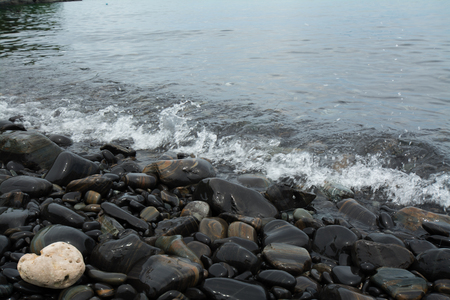 Wave hitting black stones on the beach.の写真素材