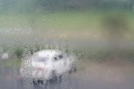 Rain drops on the window glass with blurred white car outside.の写真素材