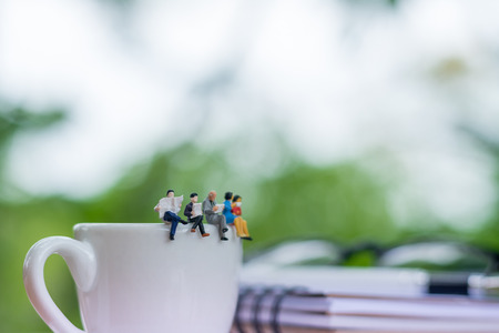 Miniature businessmans readinging book and sitting on the cup of coffee with glasses and notebook background using as a business concept.の写真素材