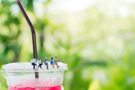 Miniature businessman and businessgirl are reading a book and sitting on the plastic cup of drink using as a business and education concept.の写真素材