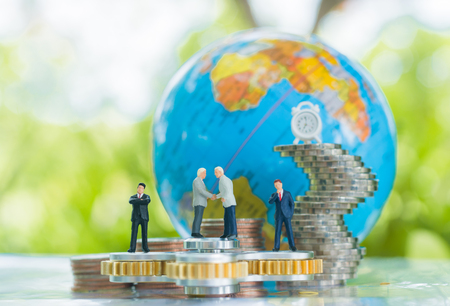 Miniature businessman handshaking on the fidget spinner with globe and growing stacks of coins background using as commitment, agreement, investment and partnership business concept.の写真素材