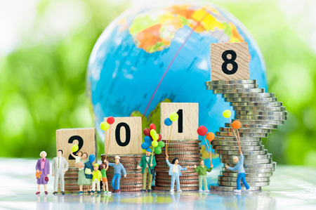 Tiny miniature model peoples of big happy family with bolloons are smiling and joying together with wooden number 2018 on growing stacks of coins and globe background, happy new year 2018 concept, business concept.の写真素材