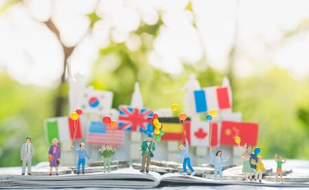 Tiny miniature model of multi-generation family holding a balloons with international flags background using as Relationship Family Generations Togetherness Concept.の写真素材