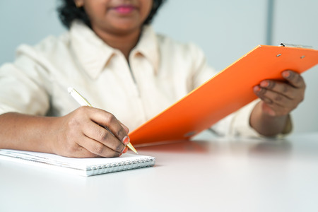 Female Asian conducting meeting or interview with clipboard and writing on note pad with pen