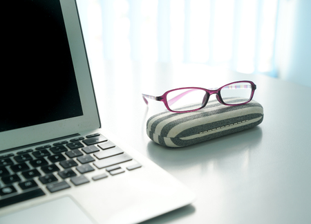 Lap top and spectacles on office desk with windows at the background
