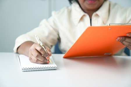 Female Asian conducting meeting or interview with clipboard and writing on note pad with pen
