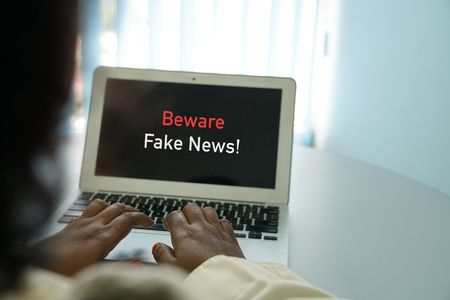 Fake news concept - female hands on laptop with words beware fake news appear on screenの写真素材