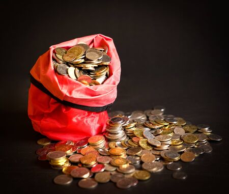 Metal coins in a red bag spilled over to the table. Dark background. Money or savings concept.の写真素材