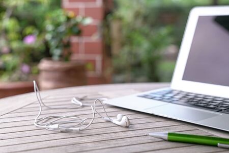 Laptop with ear phones and green pen, on light wood table. Outdoor or home office conceptの写真素材