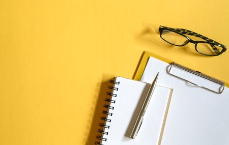 Yellow color office table top view with clipboards with paper, reading glasses, memo pad and pen....