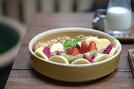 Healthy bowl of granola with berries, kiwi, banana fruit. On a wood table. Breakfast or nutritious meal concept.の写真素材