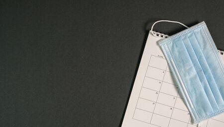 Top view of black color office table with calendar and surgical face mask. Copy space.の写真素材