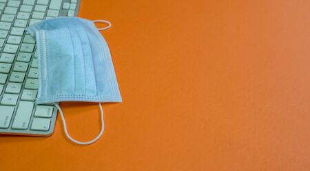 Medical face mask on top of keyboard. Orange background. Top view. Copy space.の写真素材