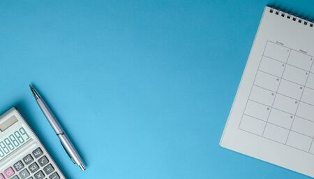 Calculator, pen and table calendar on blue background. Top view of office desk. Copy space.の写真素材