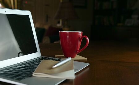 Computer laptop with notepad and focus on coffee resting on wood table. Copy space. Work at home concept.の写真素材