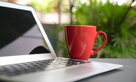 Computer laptop with offee in red cup with green nature background. Work remotely or from home. Selected focus. Copy space.の写真素材