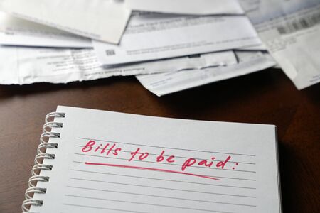 Bills to be paid, red color written words on notebook with bills and invoices at the background. Unemployment or recession concept.の写真素材