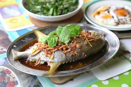 Steamed whole fish in soy sauce with ginger, garlic and mint garnish. Home cooked.の写真素材