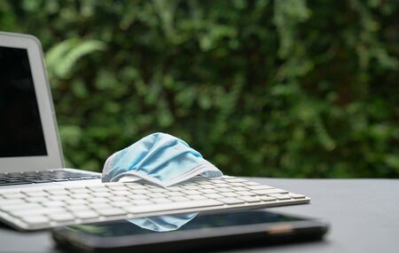 Medical face mask on top of computer laptop keyboard and cellphone. Work at home during covid-19...
