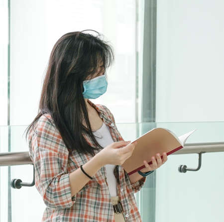 Asian woman wearing face mask reading a bookの写真素材