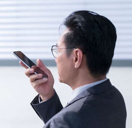 Chinese businessman using cellphone to leave voice message. Closeup, head shot.の写真素材