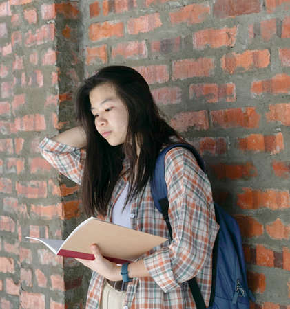 Asian woman reading a book with brick wall backgroundの写真素材