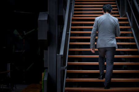 Back view of businesman with jacket walking up wooden staircase.の写真素材
