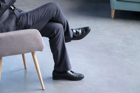 Businessman sitting on a chair, focus on legs and shoes. Modern interior surroundings. Copy space.の写真素材