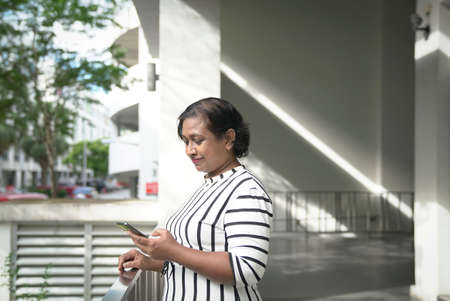 Indian business woman reading her cellphone at office corridor. Ourdoor and urban background.