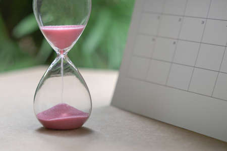 Hour glass with sand flowing, next to calendar. Time management or deadlines concept.