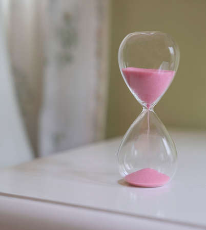 Sand glass on white table. Close up. Measuring time passing, countdown or daily routine concept.