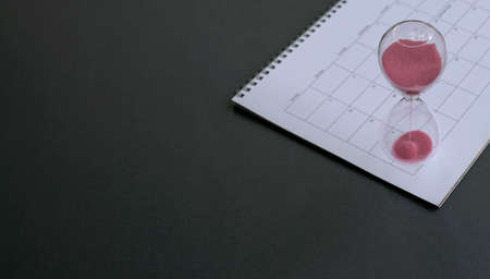 Hourglass with sand flowing, on calendar. Black top background.の写真素材