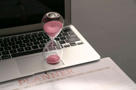 Hourglass on top of computer laptop and calendar planner. Business planning concept.の写真素材