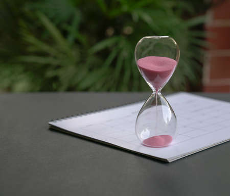 Hour glass with sand flowing,  sitting on calendar. Time passing, countdown or deadlines concept.の写真素材