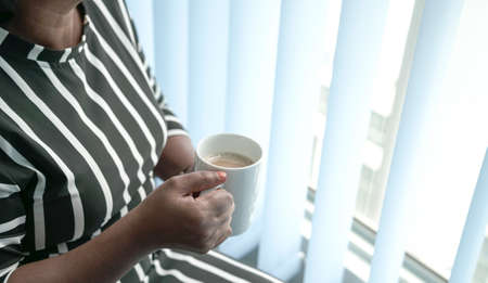 Woman holding a cup of coffee in her hands. Work place setting.の写真素材