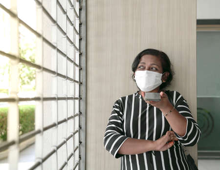 Woman wearing face mask leaning on a pillar leaving voice message on her cellphone