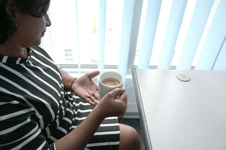 Woman holding a cup of coffee in her hands. Work place setting.