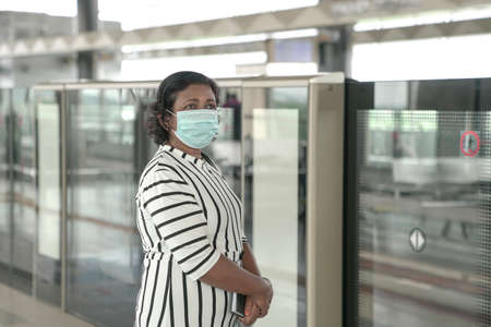 Woman wearing face mask standing and waiting for train at subway platform