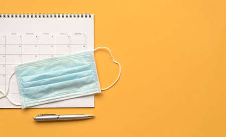 Calendar with medical face mask and pen on yellow background. Top view. Copy space.の写真素材