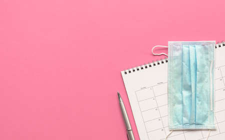 Calendar with medical face mask and pen on pink background. Top view. Copy space.の写真素材