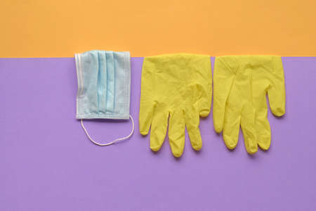 Hand gloves and medical face mask on purple  and yellow background. Top view.