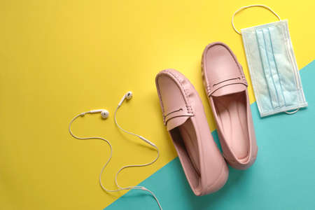 Stylish women shoes, ear phones and medical face mask on yellow and blue background. Walking outdoors with protection from virus concept.の写真素材