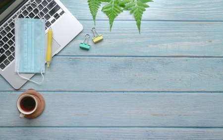 Wood table with computer laptop, face mask, coffee, supplies and green plants.の写真素材