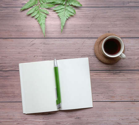 Open notepad with pen, coffee and green plants on wood table. Top view.