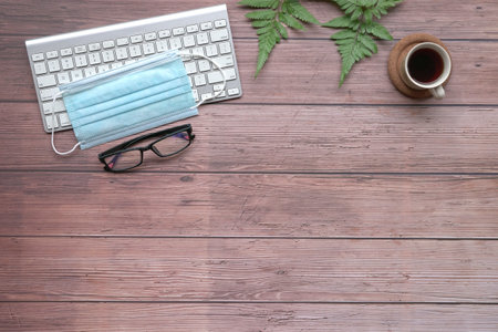 Face mask, spectacles, keyboard, coffee, plants on top of wood table. Top view.の写真素材