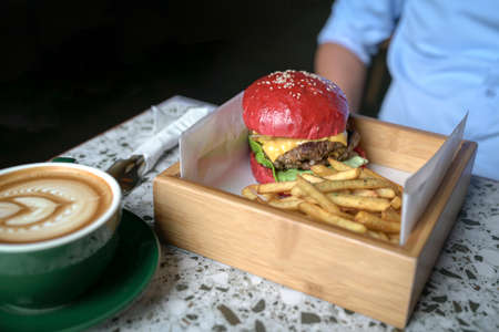 Man sitting at a table with burger, potato chips and coffee. Meal time concept.