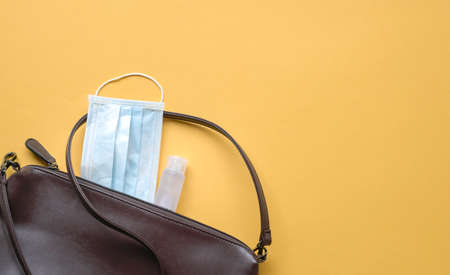 Woman pouch with face mask and hand sanitizer  on yellow background. Health and safety on the move concept.の写真素材